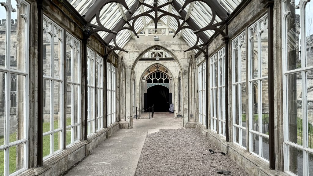 A corridor with glass windows and ceiling with a dark door at the end. 